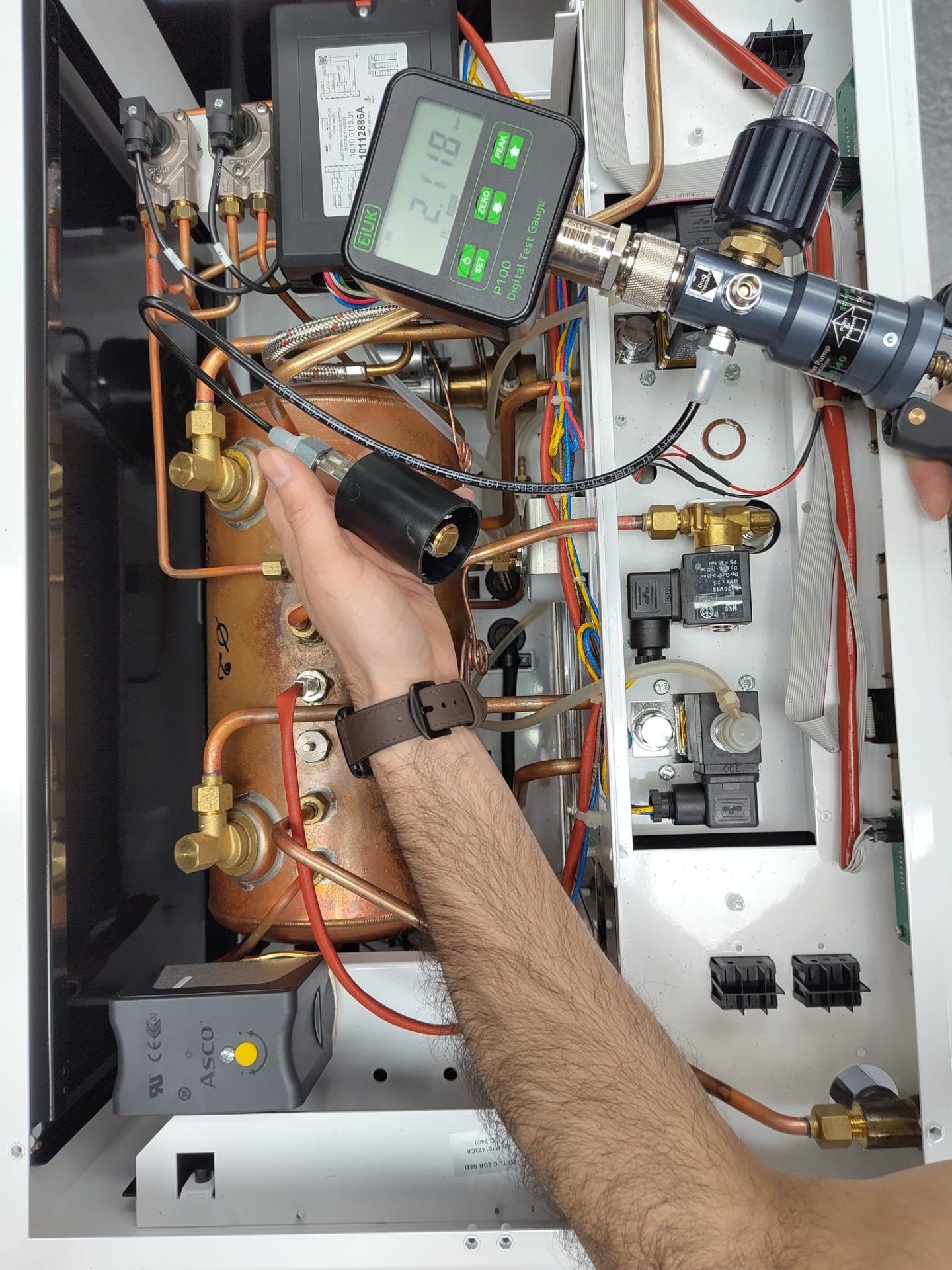 Nine Bar engineer taking a boiler pressure reading of 2.118 bar with a digital test gauge inside a commercial espresso machine